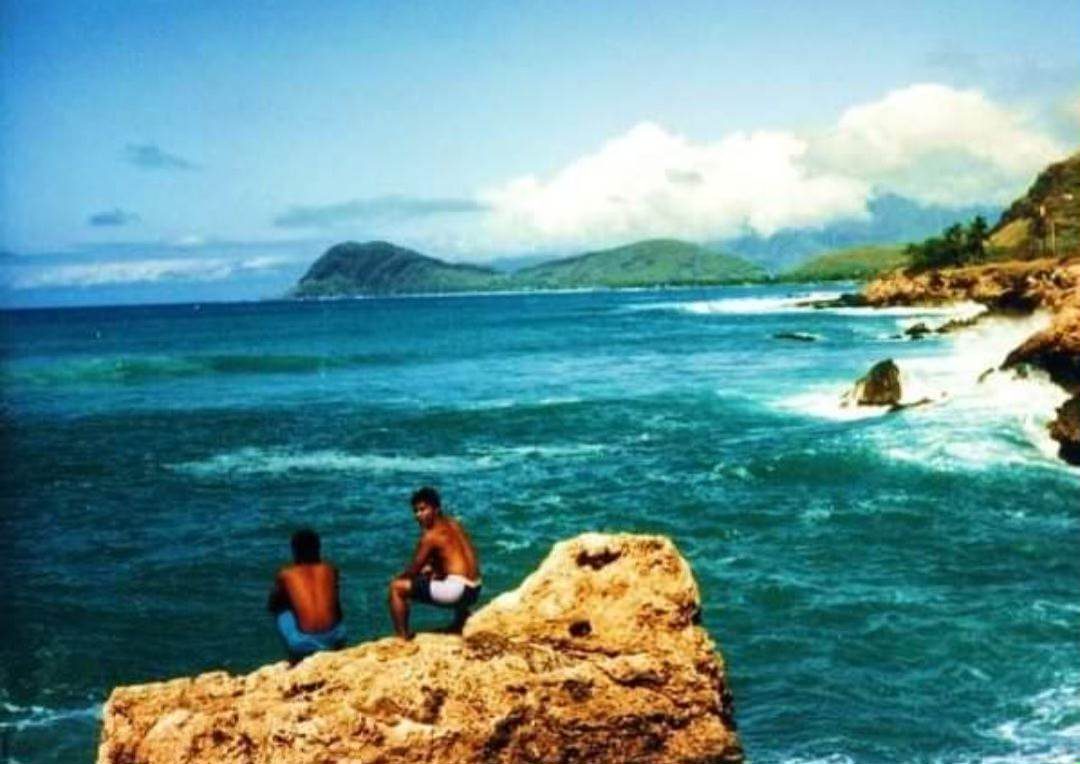 Two people sitting on the rocks above the water on the West side